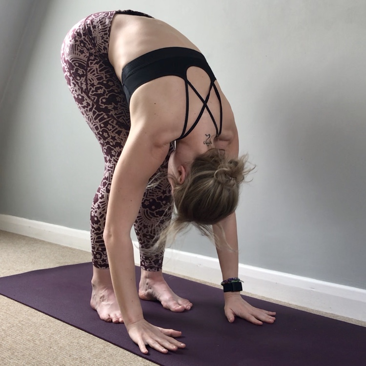 Photograph of Jade doing yoga at home in a in standing forward fold, uttanasana.