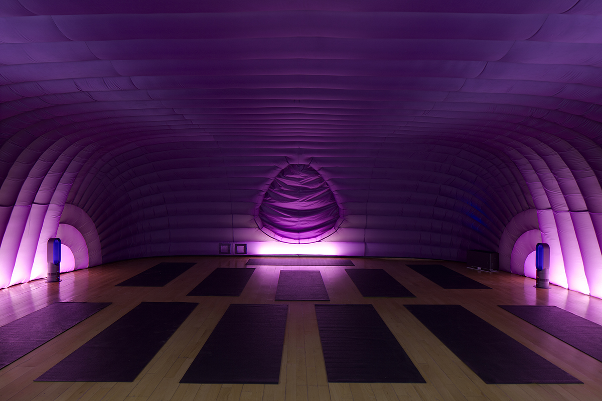 The image shows the pod of hotpod yoga, a purple inflatable room filled with yoga mats and lit at the sides.
